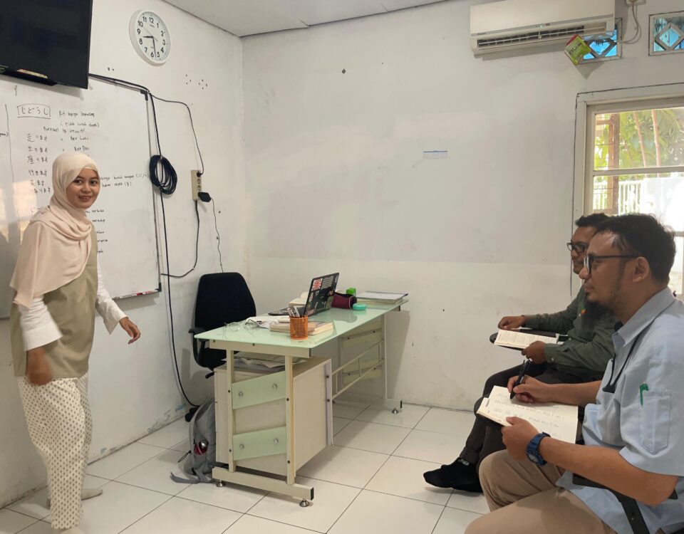 Seorang pengajar sedang memberikan pelatihan bahasa Jepang kepada dua staf perusahaan dalam kelas khusus persiapan rotasi ke Jepang.