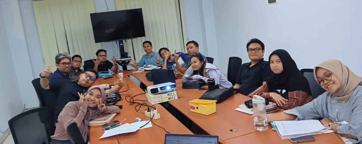 Peserta pelatihan bahasa Jepang in house duduk di ruang rapat, berpose santai bersama instruktur di tengah sesi pelatihan di perusahaan manufaktur.
