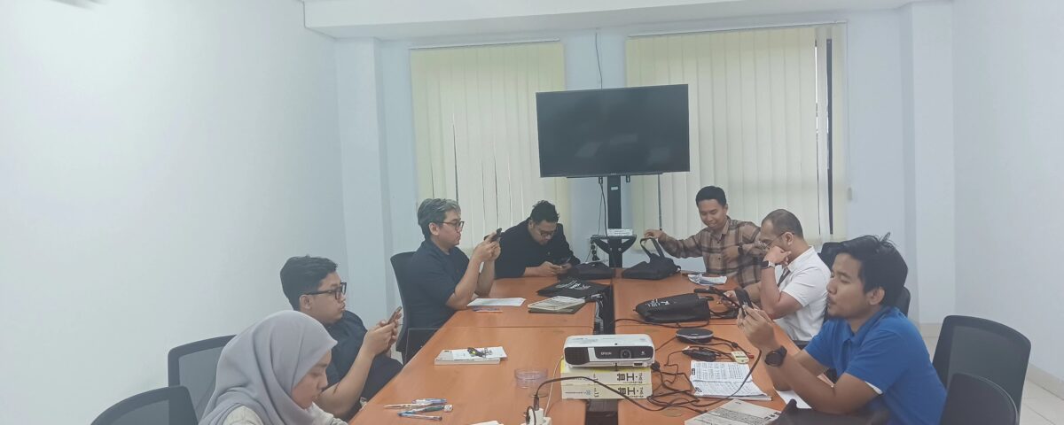 Peserta pelatihan bahasa Jepang on site duduk di ruang rapat perusahaan, mempelajari materi menggunakan ponsel dan buku pelajaran.