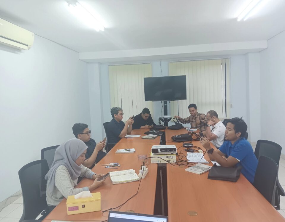 Peserta pelatihan bahasa Jepang on site duduk di ruang rapat perusahaan, mempelajari materi menggunakan ponsel dan buku pelajaran.