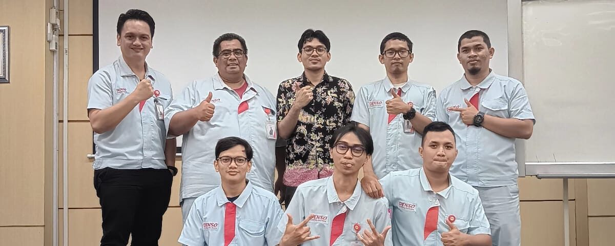 Peserta training bahasa Jepang di pabrik berfoto bersama instruktur setelah sesi pelatihan di lingkungan kerja manufaktur.
