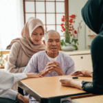 Seorang pekerja perawatan Indonesia berhijab sedang berinteraksi dengan seorang lansia Jepang di sebuah ruangan dengan elemen tradisional Jepang.