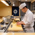 Seorang koki sushi muda terampil sedang menyiapkan sushi di balik konter sushi yang bersih di sebuah restoran di Tokyo.