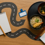 Foto flat lay realistik menampilkan ilustrasi roadmap keterampilan pelayan restoran Jepang dengan jalur jalan berliku di atas meja kayu, mengarah pada set hidangan udon, tempura, dan sup miso. Terlihat pula buku catatan, pensil, sumpit kayu, dan aksen merah halus, menggambarkan proses pembelajaran dan karir di bidang kuliner Jepang.