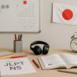 Strategi persiapan JLPT N5–N4 jelang jadwal JLPT Desember 2025—setup belajar realistis tanpa manusia dengan aksen abu-abu dan merah.